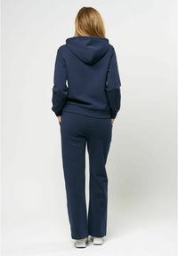 Tumši zilas krāsas kapucīte ar regulējamu kapuci, apvienota ar saderīgām izplatītām biksēm. Audums, šķiet, ir gluds un elastīgs, ideāli piemērots neformālai valkāšanai.