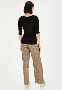 Czarny dopasowany top z marszczonymi rękawami, zestawiony z brązowymi spodniami w kratę o szerokich nogawkach i beżowymi butami na platformie. Prosty i nowoczesny design.