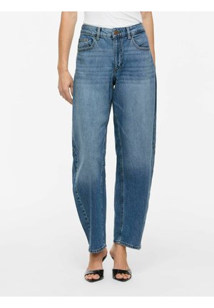 Kvinde iført højtaljede, løstsiddende blå jeans med forlommer og en hvid top, parret med sorte åbne hæle på en hvid baggrund.