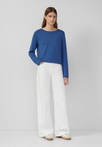 Blaues Langarmoberteil mit rundem Ausschnitt, kombiniert mit weit geschnittenen weißen Hosen. Das Outfit zeichnet sich durch ein einfaches Design und weiche Texturen aus.