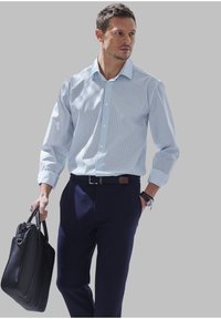 Camicia button-up azzurro chiaro con un motivo sottile, maniche lunghe, abbinata a pantaloni scuri blu navy e una borsa in pelle nera.