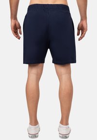 Pantaloni corti blu navy con vita elasticizzata, tasche laterali e tessuto leggero. Indossati con sneakers bianche con testo nero.
