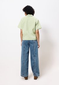 Grün-weißer kariertes Kurzarmhemd, das mit lockeren blauen Jeans-Hosen im weiten Schnitt kombiniert wird, die sichtbare Nähte und ein lässiges Design aufweisen.