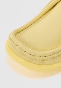 Pantofii din piele galbenă au vârful rotund, o talpă robustă și cusături vizibile pe margine, evidențiind o textură netedă.