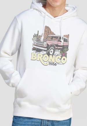 White hoodie with a vintage pink Bronco vehicle illustration, desert cactus and rock formations, text "BRONCO 1966" on front.