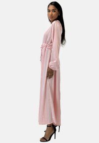 Lång, rosa satin klänning med åtsittande midja, långa ärmar och en sidoslits. Kombinerad med svarta, strappy högklackade sandaler.