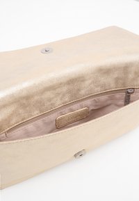 Zlaté kovové psaníčko s hladkou texturou, zapínáním na zacvaknutí a vnitřní kapsou na zip s označením značky.