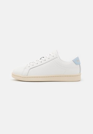 Weißer niedriger Sneaker mit beiger Sohle und hellblauem Fersenlasche, mit weißen Schnürsenkeln und minimalen Nahtdetails, seitlich gezeigt.