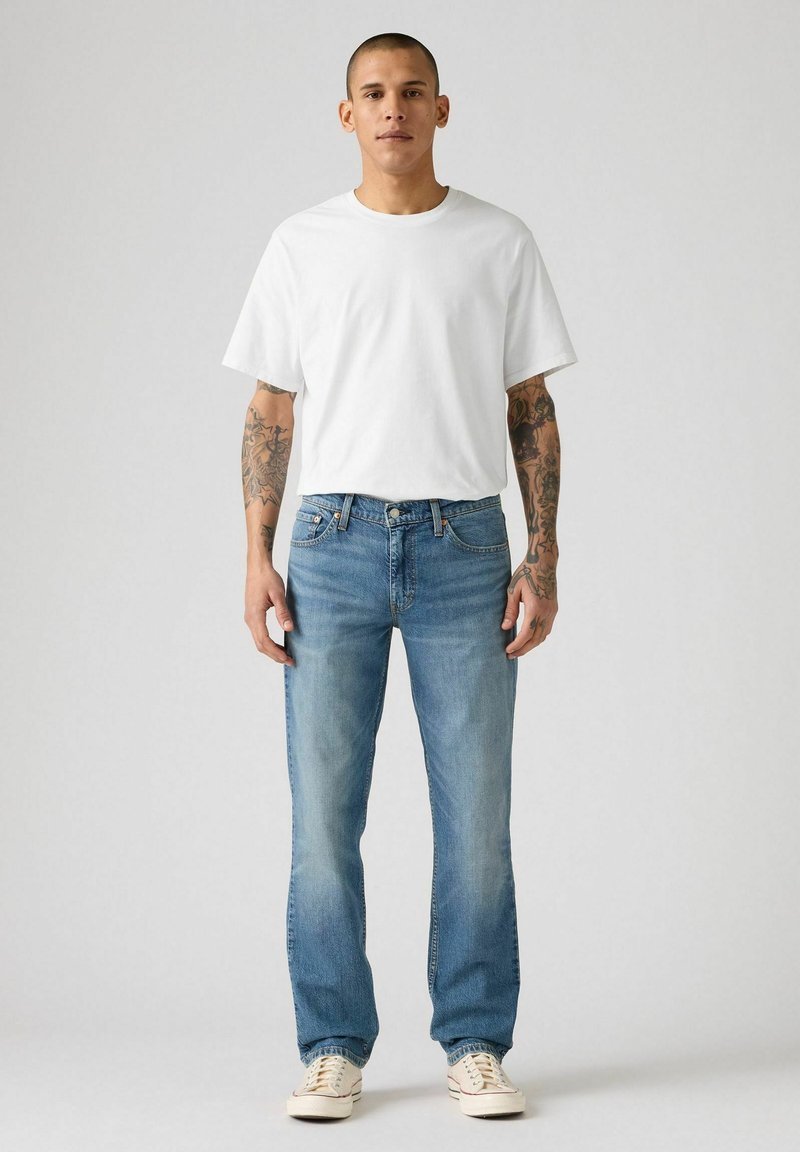 Weißes Baumwoll-T-Shirt kombiniert mit hellblauen Denim-Jeans. Die Jeans verfügen über ein klassisches Fünf-Taschen-Design. Die Sneakers sind beige mit weißen Schnürsenkeln.