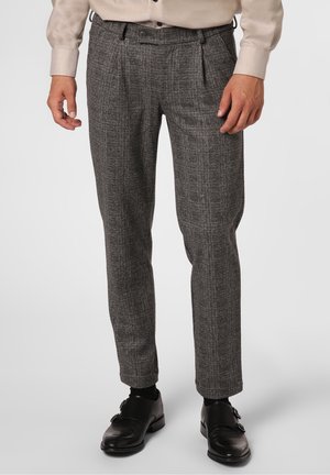 Mand iført gråternede bukser, sorte læder sko med dobbelt monkstrap og en lysefarvet langærmet skjorte.