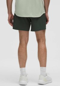 Dunkelgrüne sportliche Shorts für Herren mit glatter Textur, kombiniert mit weißen Schuhen und Socken, von hinten betrachtet.