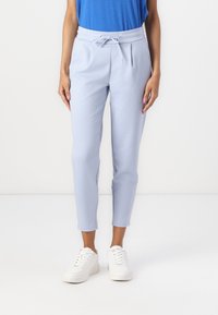 Lyseblå bukser med elastisk linning og snor. Har slim fit og smale ben. Kombinert med hvite joggesko.