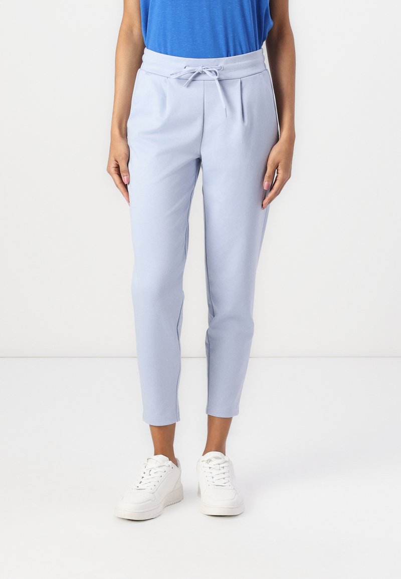 Lyseblå bukser med elastisk linning og snor. Har slim fit og smale ben. Kombinert med hvite joggesko.