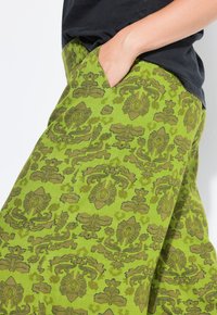 Groene patroonrok met een bloemendessin, zijkleine zakken en een soepele textuur. De stof heeft een contrasterend donkerder groen patroon.