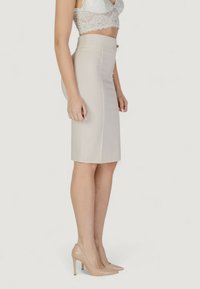 Falda lápiz beige hecha de una tela suave, con una cintura alta y un cierre de cremallera en la parte posterior. Combinada con tacones altos nude.