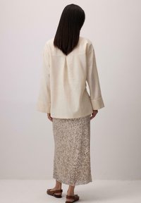 Cămașă din in de culoare albă murdară, de croială lejeră, cu mâneci largi; fustă bej cu paiete, până la genunchi, cu detalii strălucitoare verticale; sandale maronii.