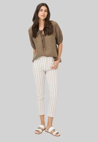 Khaki linnen blouse met pofmouwen en een strikhalslijn, gecombineerd met wit gestreepte cropped broek en witte slide sandaal. Glad textuur.