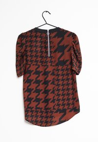 Blouse à motif pied-de-poule marron et noir avec manches courtes bouffantes et fermeture éclair dans le dos ; tissu lisse et ourlet arrondi.