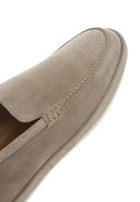 Zapato slip-on de ante beige con puntera redondeada, detalle de cosido mínimo y textura suave. Suela blanca con patrón de surcos sutil.