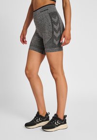 Shorts sportivi grigi con una vita larga, tessuto testurizzato e un motivo a chevron a contrasto sui lati. Indossati con scarpe da ginnastica nere.