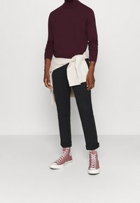 Bordowy golf, jasno kremowa bluza przewiązana w talii, czarne spodnie i różowe trampki za kostkę z białymi podeszwami.