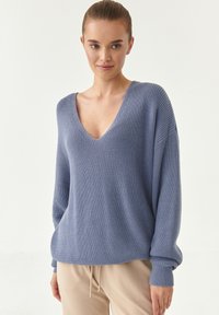 Maglione azzurro chiaro lavorato a maglia con scollo a V profondo, maniche lunghe e texture a coste. Il tessuto morbido scivola liberamente sul corpo.