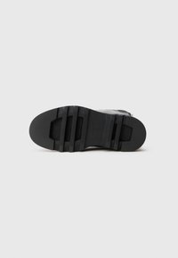 Suela de zapato de goma negra con superficie texturizada, que presenta surcos y estrías. Forma clásica con contorno suave, diseñada para ofrecer tracción.