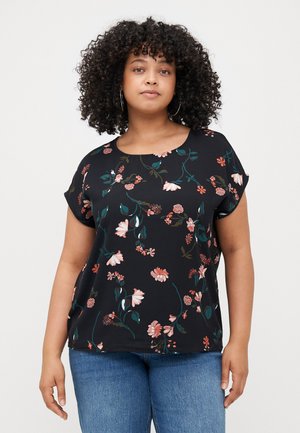 Svart blomstret topp med scoop-hals, korte ermer, med rosa og grønne blomsterdesign, iført lyseblå bukser.