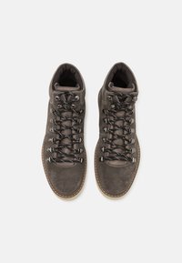 Botas de senderismo de ante marrón con cordones negros, suela de goma y cuello acolchado. Textura suave con costuras en contraste y ojales de metal.