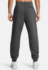 Pantalones deportivos grises con cintura elástica, puños ajustados y un bolsillo trasero. Hechos de un tejido suave con una textura lisa.