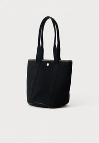 Černá taška na rameno s dlouhými textilními ušima, bílým prošíváním nahoře a malým kulatým zlatým knoflíkem uprostřed vpředu.