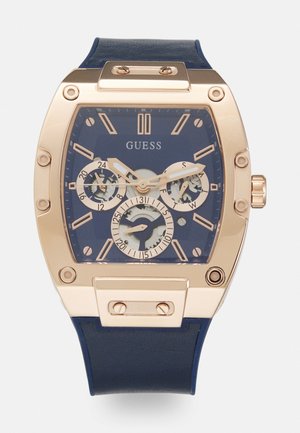 Montre à bracelet en cuir bleu avec un boîtier rectangulaire en métal doré, un cadran bleu, trois sous-cadrans et des accents argentés pour les indicateurs des heures et des minutes.