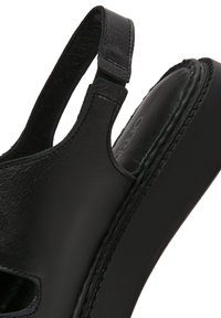 Sandalia de cuero negro con un diseño abierto, correa ajustable, plantilla acolchada y detalles de costura en los bordes.