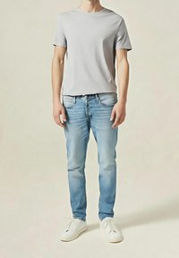 Harmaa lyhythihainen t-paita yhdistettynä vaaleansinisihin kapealahkeisiin farkkuihin ja valkoisiin lenkkareihin. Sileä kangas, rento malli, ei näkyviä kuvioita.