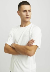 Valge lühikeste varrukatega sportlik T-särk struktuurse mustriga. Ees on peen "CNZ" logo. Raglan varrukad, vabalt langev lõige.
