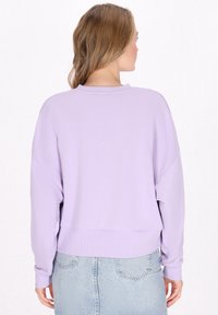 Felpa pullover lavanda con vestibilità rilassata, spalle scese, polsini a costine e orlo cropped. Tessuto morbido, dettagli di design minimal.