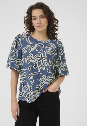 Blauses Hemd mit floralem Muster in Blau und kurzen Puffärmeln, locker geschnitten und mit weichem Stoff, kombiniert mit schwarzen Hosen.