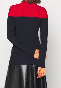 Pull côtelé bleu marine avec une section supérieure à rayures rouges unies. Col montant et manches longues, associé à une jupe en cuir noire.