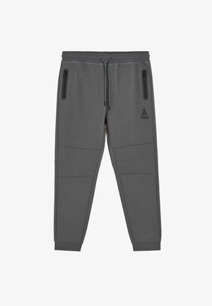 Szare spodnie sportowe o tapered fit, z dwiema kieszeniami na zamek i ściągaczami przy kostkach. Posiadają przeszywane panele oraz logo na biodrze.