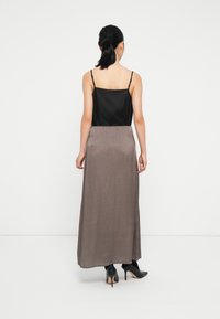 Svart sateng-camisole med tynne stropper, paret med et langt, brunt teksturert skjørt og svarte høyhælte sko. Enkelt design, ingen mønstre.