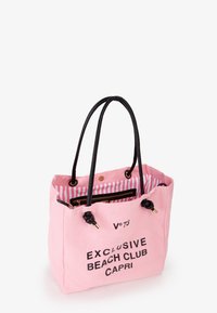 Roze canvas draagtas met zwarte handvatten, voorzien van een gestreepte binnenvoering en bedrukte tekst: "EXCLUSIEVE STRANDBEDELDING CAPRI." Gouden accenten opgemerkt.