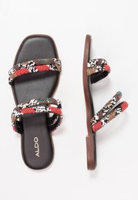 Pärlade flatsandaler med två breda remmar i mönster av röd, svart, vit och brun, läderfotbädd och platt brun sula. Varumärket synligt.