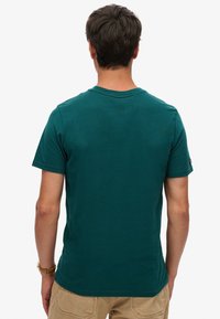 Camiseta de algodón en color verde azulado con mangas cortas, cuello redondo y una etiqueta en el hombro izquierdo. Textura suave y diseño ajustado.