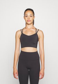 Zwarte sportbeha met dunne verstelbare bandjes, een V-vormige halslijn en een gladde textuur, gecombineerd met hoge zwarte leggings.