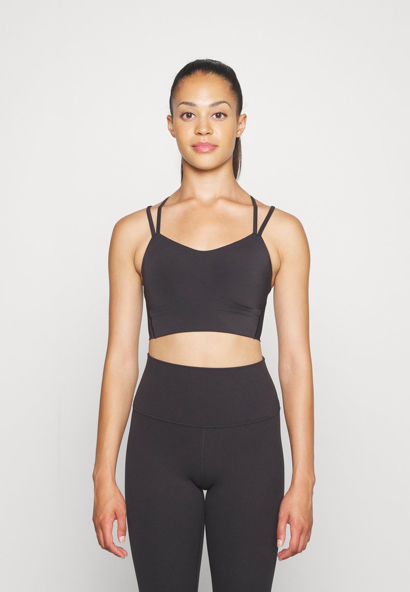 Zwarte sportbeha met dunne verstelbare bandjes, een V-vormige halslijn en een gladde textuur, gecombineerd met hoge zwarte leggings.