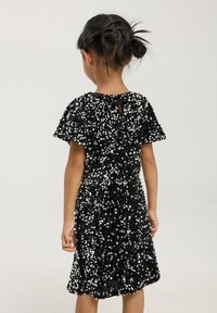 Abito nero coperto di paillettes riflettenti, con maniche a sbuffo, scollatura tondeggiante e apertura a chiave sul retro.