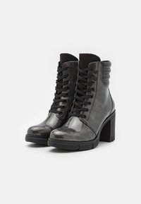 Botas de tobillo negras con un acabado brillante, con punta redonda, diseño con cordones y un tacón grueso. Detalles acanalados en la parte trasera.