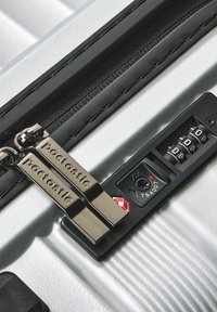 Maleta dura plateada con superficie texturizada, que cuenta con cremalleras dobles, un candado con combinación aprobado por la TSA y acentos negros.