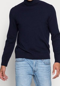 Mörkblå polotröja i mjukt stickat material, med en åtsittande design och ribbade mudd och nederkant. Matchas med ljusblå jeans.