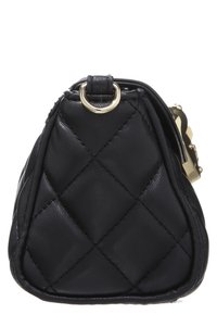 Svart quiltad läderhandväska i profil med en guldfärgad metallring och delvis guldspänne synligt på vit bakgrund.